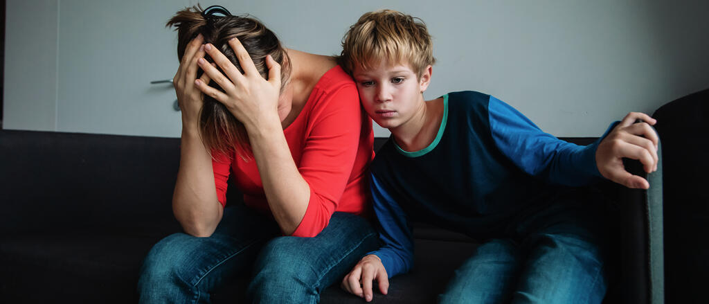 Ein Kind mit traurigem Gesichtsausdruck lehnt sich an seine Mutter an Kinder psychisch kranker Eltern